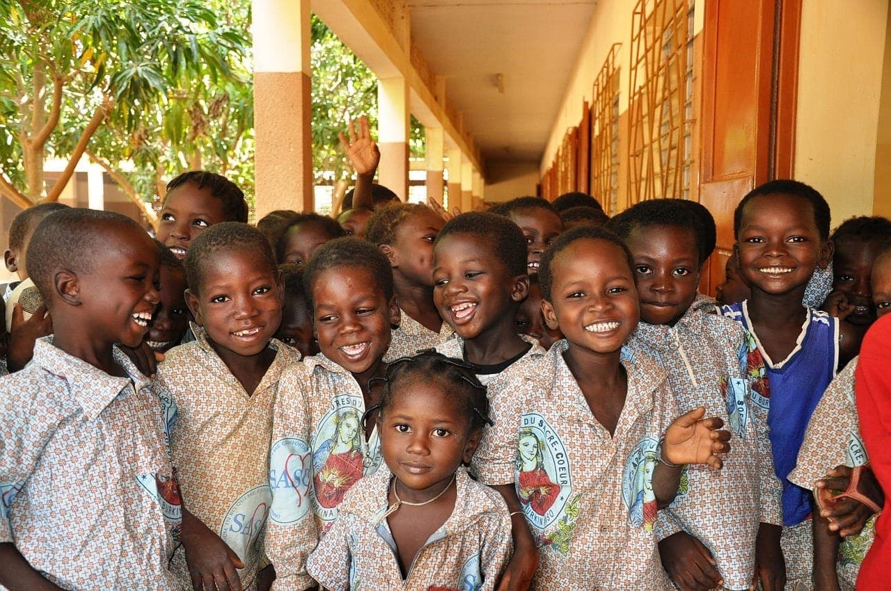 Un groupe d'écoliers et d'écolières serrés les uns contre les autres rient aux éclats sous l'auvent d'une école