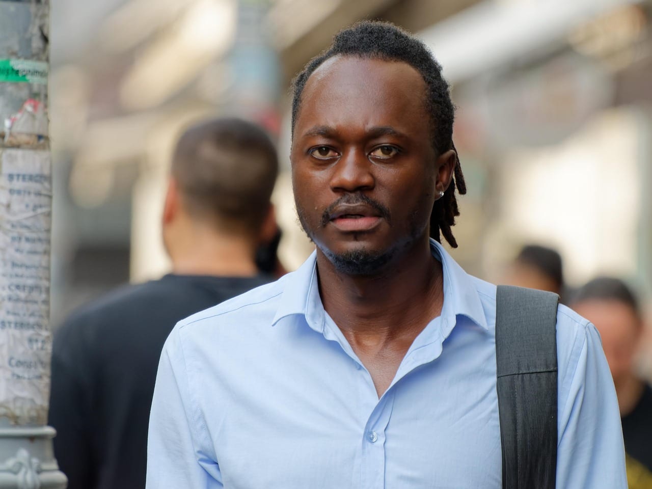 Un homme en chemise bleu clair, sacoche à l'épaule, le regard soucieux, au milieu de la foule d'une rue animée