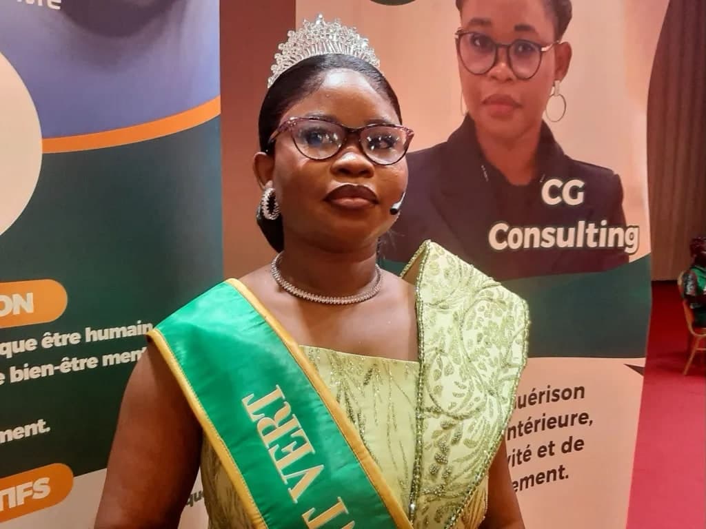 Coach Christelle Gnimassou, promotrice du CIGIBM, en tenue verte avec diadème et écharpe, devant les panneaux du congrès