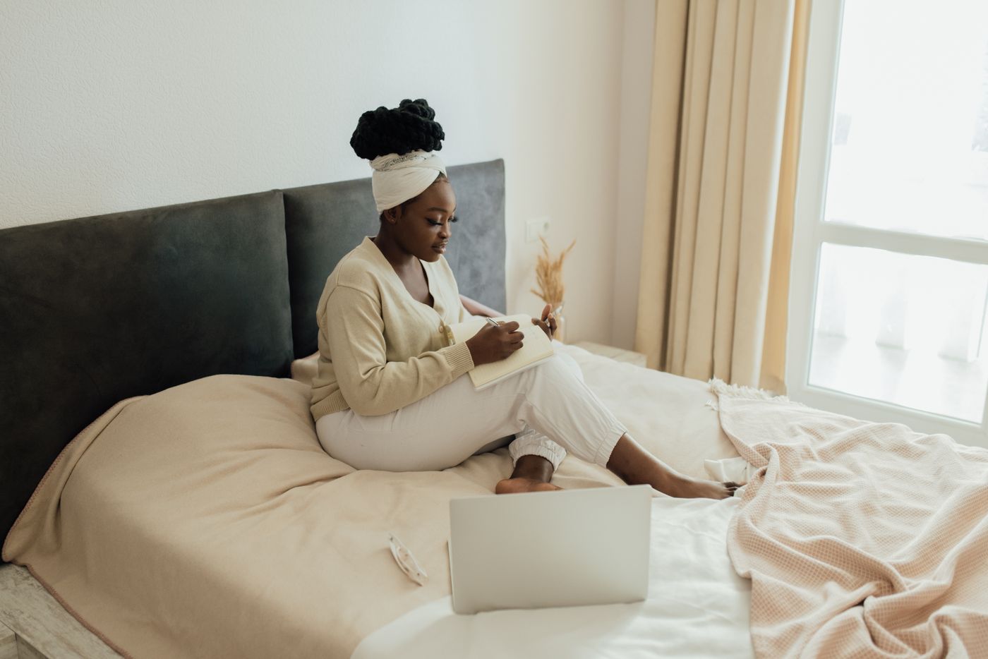 Femme assise sur son lit, en train d'écrire dans un carnet, lumière du matin